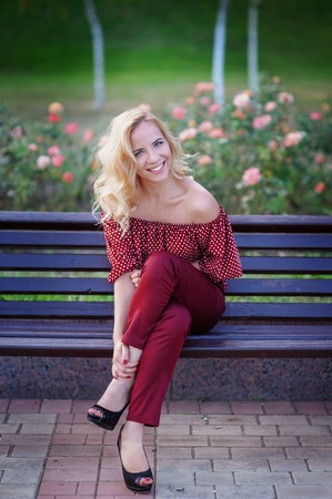 beautiful blonde woman sitting on a bench in the parkの写真素材