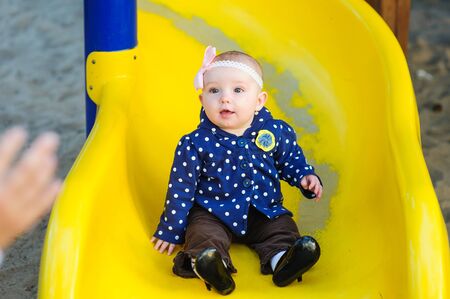 little baby girl slides down on the yellow game hillの写真素材