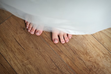 bride legs with a pedicure and a wedding dress in the wedding morningの写真素材