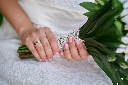 Hands of the bride with a gold ring hold a wedding bouquetの写真素材
