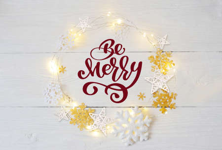 Text Be Merry in a Christmas with garlands and snowflakes on a wooden background.