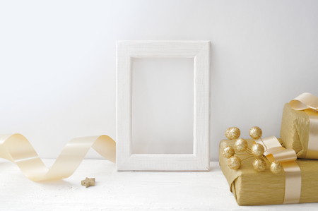 Mockup Christmas white frame with a golden ribbon and a gift, flatlay on a white wooden background, with place for your textの写真素材