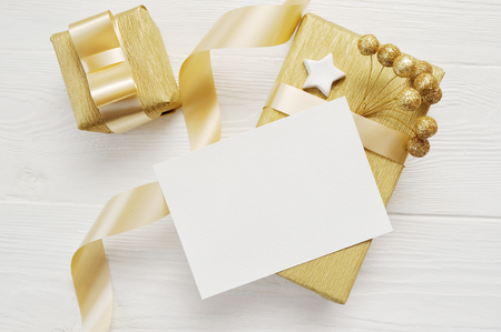 Mockup Christmas greeting card with gold gift ribbon, flatlay on a white wooden background, with place for your textの写真素材
