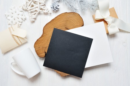 Mockup Christmas black greeting card letter in envelope and mug, flatlay on a white wooden background, with place for your text. Flat lay, top view photo mock upの写真素材