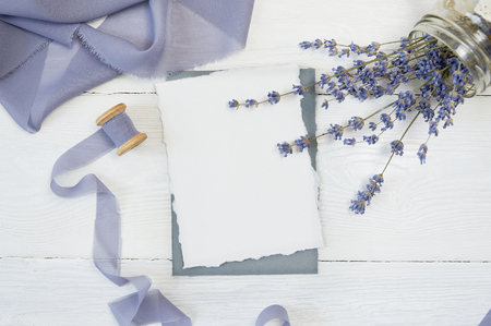 White blank card on a background of blue ribbon with lavender flowers on a white background. Mockup with envelope and blank card. Flat lay. Top viewの写真素材