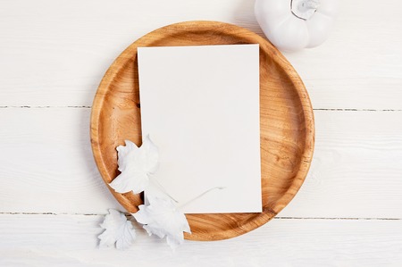 Wooden place with white sheet of paper. White pumpkin, berries and leaves on a mockup autumn wooden background. Greeting card for Thanksgiving Day in rustic style with space for your text. Flat lay. Top viewの写真素材