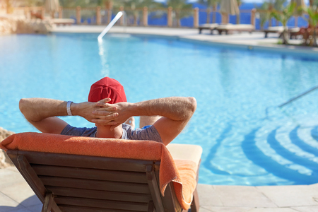 Positive man in red hat resting near the swimming pool hotel in Egypt. Concept beautiful lifestyleの写真素材