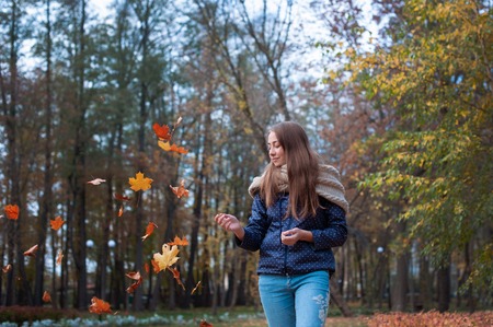 Outdoors lifestyle fashion image of happy beautiful girl throwing leaves up in the air in autumn...