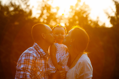 Happy family in the park evening light. The lights of a sun. Mom, dad and baby happy walk at sunset. The concept of a happy family.の写真素材