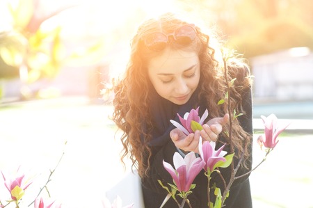 Young woman near blossoming magnolia flowers tree in spring park on sunny day. Beautiful happy girl enjoying smell in a flowering spring garden.の写真素材