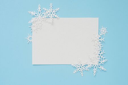 Christmas or winter composition. Frame of white snowflakes and white sheep of paper on pastel blue background. Christmas winter, new year concept. Flat lay, top view copy spaceの写真素材