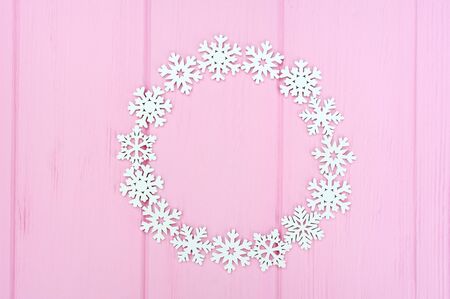 Holiday round frame made of christmas white snowflakes on pink wooden background. Composition with place for text. Flat lay, top viewの写真素材