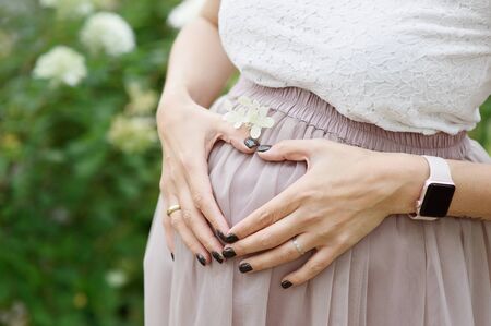 woman makes a heart shape with her hands over her expanding waistline, her navel centered. Flowers...