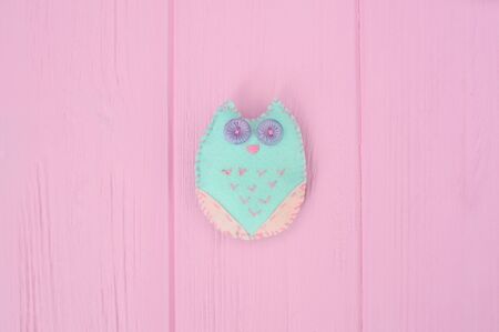 Self-made soft toy owl made of felt crafts on a pink wooden backgroundの写真素材