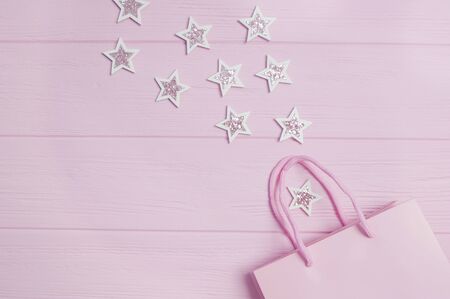 Christmas New Year flat lay mock up and Birthday congratulations Top view pink gift bag and glitter confetti in the form of stars on pink wooden background. Greeting card Festive holiday pastel backdropの写真素材