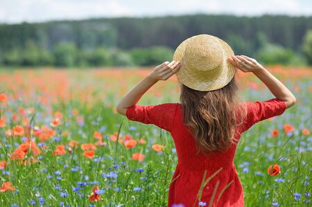 Dreamy woman in red dress and hat in beautiful herb flowering poppy field. Vintage elegant romantic look. concept of lovely summer.の写真素材