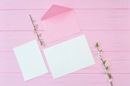 Two branches of white cherry flowers on pink wooden background with mockup sheet of papers and...