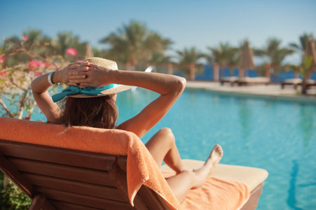 Woman in a straw hat relaxing on a daybed near a luxurious summer pool hotel Egypt, concept time to travelの写真素材