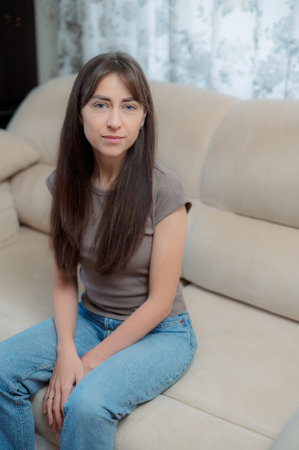 peace woman sitting comfortably on a gray couch at home, smiling and relaxing in soft natural light during the afternoonの写真素材