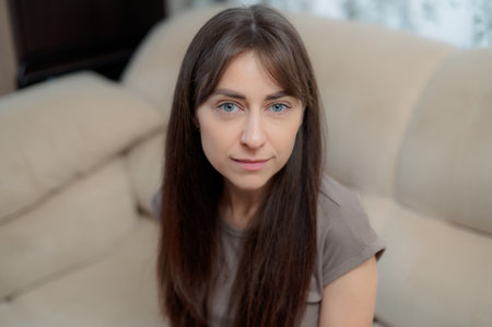 peace woman sitting comfortably on a gray couch at home, smiling and relaxing in soft natural light during the afternoonの写真素材