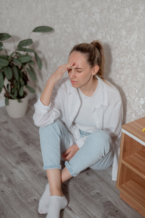 Young woman experiencing headache while sitting on a couch in a modern living room home during daytime vertical photoの写真素材