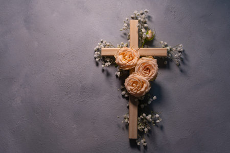 Simple wooden cross decorated with beautiful pink roses and white gypsophila flowers, shadow hanging...
