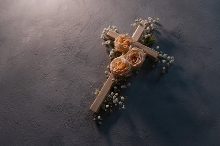 Simple wooden cross decorated with beautiful pink roses and white gypsophila flowers, shadow hanging...