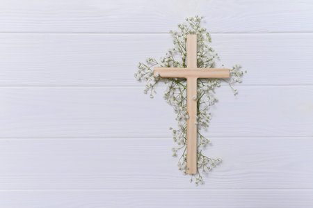 Christian wooden cross adorned with delicate white baby's breath flowers moving slowly on a white...