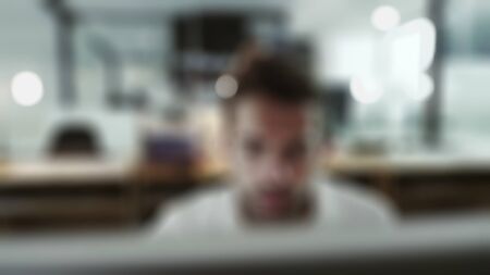 Young attractive businessman happy and successful at work at computer desk satisfied and smiling relaxed leaning on chair in front of office window  with blurry view.の写真素材