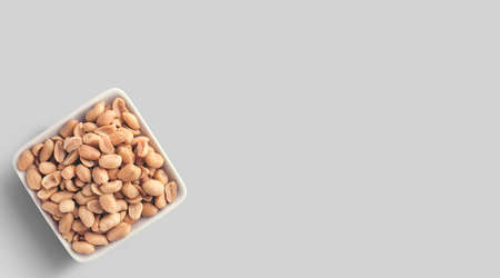 Peanuts in ceramic bowl isolated over white textured background, top view, close-up.