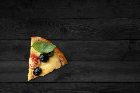Close up view of pizza with melted cheese isolated on black wooden table.の写真素材