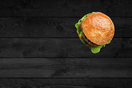 Close up view of big hamburger isolated on black wooden table.の写真素材