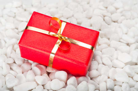 Small red and gold gift box on a background of white stonesの写真素材