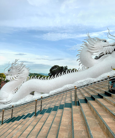 Big Twin Dragon statue at the feet of Guan Yin Buddha statue with its holy white temple, sitting on the hill mountain top or summit, at Temple or Mercy, Chiang Rai Thailand.の写真素材