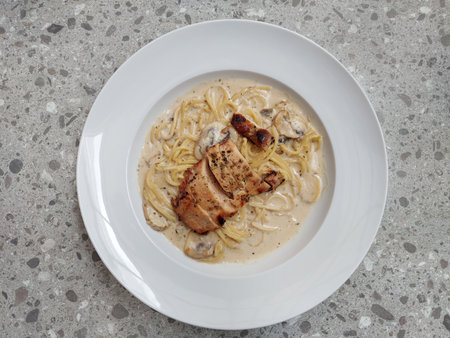 Spaghetti chicken alfredo served on a pasta plate on top of grey terrazzo table. A creamy mushroom chicken alfredo served with truffle and olive oil, parmesan cheese, and Italian hの写真素材