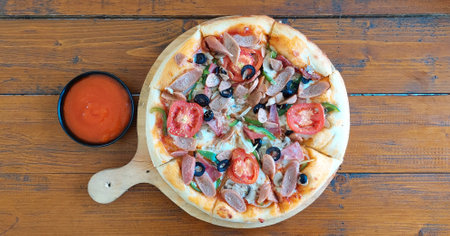 Mixed Meat pizza with cut tomatoes, paprica, onion, and black olives topping, with hot chili dipping sauce, served on a wooden rustic tableの写真素材