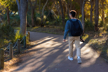 A young man using sweater walking in a park holding a camera in autumn.の写真素材