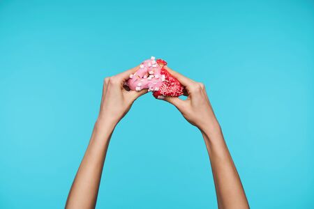 Photo of young woman's attractive hands keeping her hands raised with pink donuts in it, smashing...