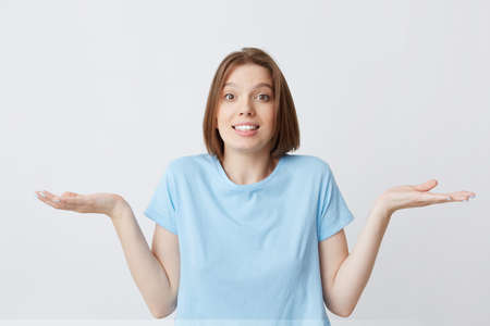Cheerful beautiful young woman in blue t shirt laughing and showing tiny size by fingers of her hand isolated over white backgroundの写真素材