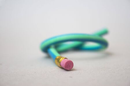 A green and blue striped rubber pencil tied in knot against gray backgroundの写真素材