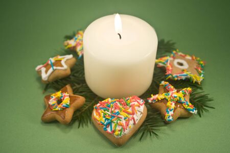 White pillar candle on fir branches surrounded by decorated gingerbread cookies on green backgroundの写真素材