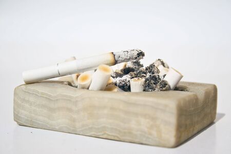 Close-up of a white stone square ashtray full of burnt cigarette buttsの写真素材
