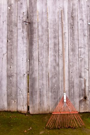 Used old flexible fork rake propped against a weathered gray wooden fenceの写真素材