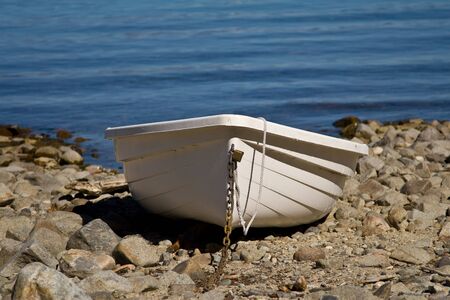 Single plastic boat beached on rocky beachの写真素材
