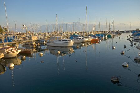 Boats and yachts in the docks at Vidy, Switzerland on Lake Geneva with the Alps in backgroundの写真素材
