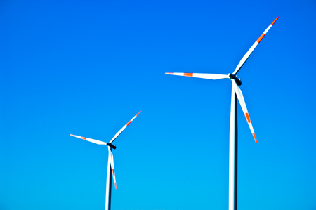 Two electricity generating windmills against a blue sky.