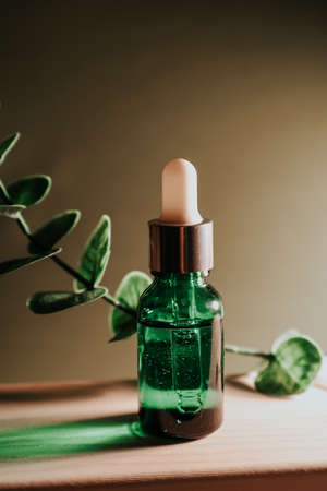 Cosmetic liquid in a clear, glass, green bottle. A sprig of eucalyptus completes the photo.の写真素材