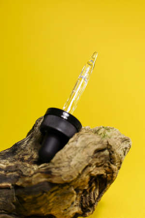 Pipette filled with cosmetics standing on a wooden stand on a yellow backgroundの写真素材