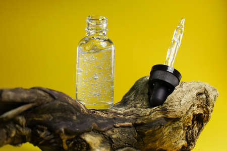 An open pipette bottle filled with clear liquid with bubbles standing on a wooden podium on a yellow backgroundの写真素材