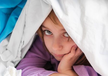 Little girl hiding under the blanket and refuses to get upの写真素材